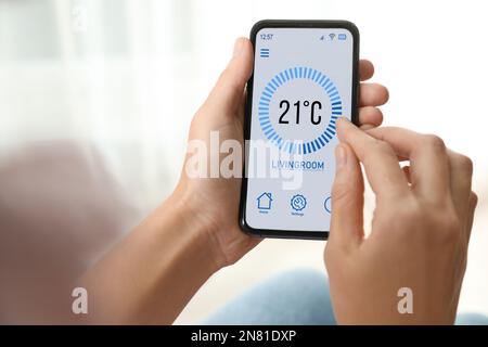 Woman using smartphone to control heating system in house, closeup Stock Photo