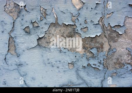 The gray flat concrete wall painted long ago with blue, light blue paint has already cracked, deep cracks on the wall are visible Stock Photo