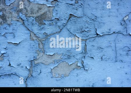 The gray flat concrete wall painted long ago with blue, light blue paint has already cracked, deep cracks on the wall are visible Stock Photo