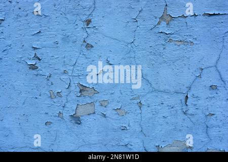 The gray flat concrete wall painted long ago with blue, light blue paint has already cracked, deep cracks on the wall are visible Stock Photo