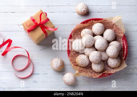 Christmas homemade gingerbread cookies sprinkled with powdered sugar on red plate on light blue background with gift wrapped in craft paper with red r Stock Photo