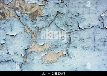 The gray flat concrete wall painted long ago with blue, light blue paint has already cracked, deep cracks on the wall are visible Stock Photo