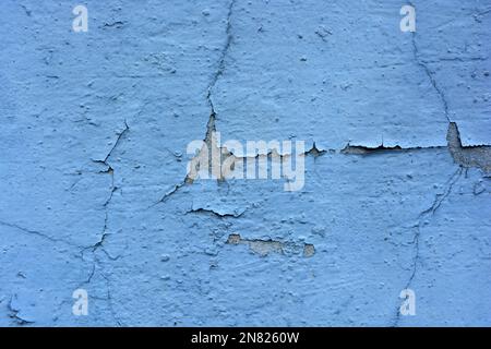 The gray flat concrete wall painted long ago with blue, light blue paint has already cracked, deep cracks on the wall are visible Stock Photo
