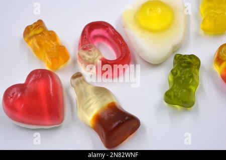 Fried scrambled eggs, a bottle of cola, colored bears, rings with stones, a pink heart are located chaotically on a white background. Stock Photo