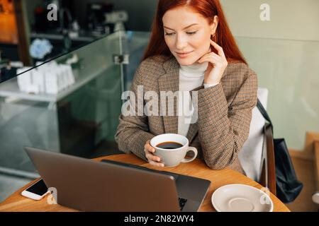 Businesswoman holding a cup of coffee and looking at laptop while sitting in cafe Stock Photo