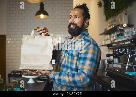 Cafe, takeaway bag and cashier man or small business owner with sustainable restaurant in customer services. Costa Rica employee, waiter or person Stock Photo
