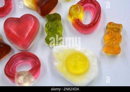Fried scrambled eggs, a bottle of cola, colored bears, rings with stones, a pink heart are located chaotically on a white background. Stock Photo