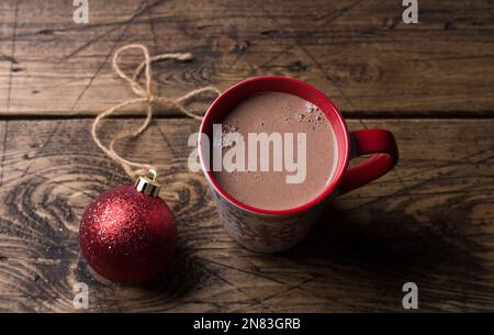 Delicious hot chocolate cocoa drink in red mug with christmas red ball on wooden background, traditional winter drink, top view Stock Photo