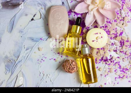 Beautiful composition of yellow cosmetic liquid face body essential oil bottles, sea salt, soap bars, lotus flower on brush strokes surface flatly. Sp Stock Photo