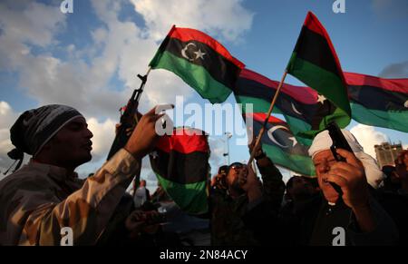 Libyans wave the national flags as they chant pro-revolutionary slogans ...
