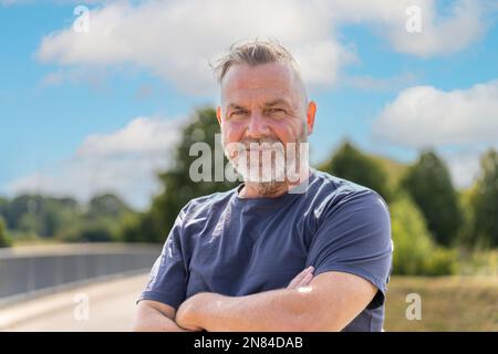 Elderly nice man standing on a bridge with crossed arms and blue sky Stock Photo