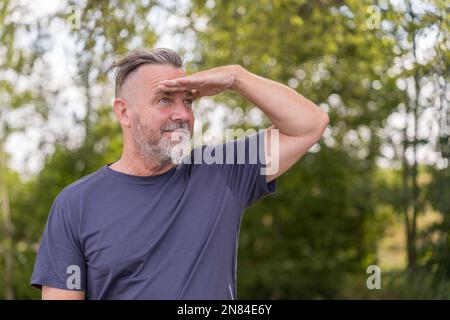 Pensive middle aged man with his hand to his forehead looking into the distance outside against a green background Stock Photo