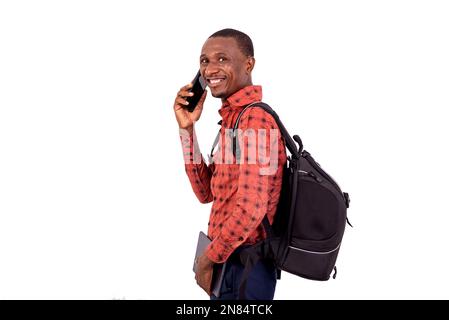 young male student with a backpack talking on mobile phone while smiling at the camera. Stock Photo