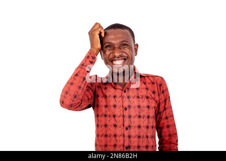 a young man in a checkered shirt standing on a white background scratching his head laughing. Stock Photo