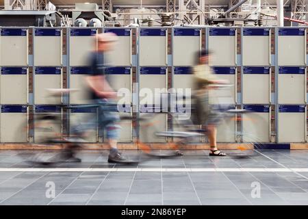 blurred people with bicycles walking in front of left luggage lockers Stock Photo