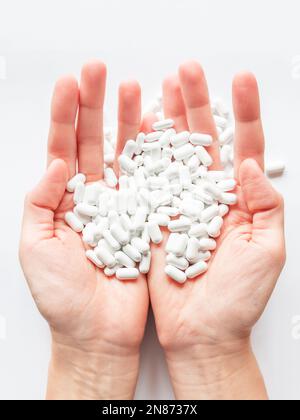 Palm hands full of white scattering pills. Woman gripes hand with capsules with medicines on light background. Flat lay, top view. Stock Photo