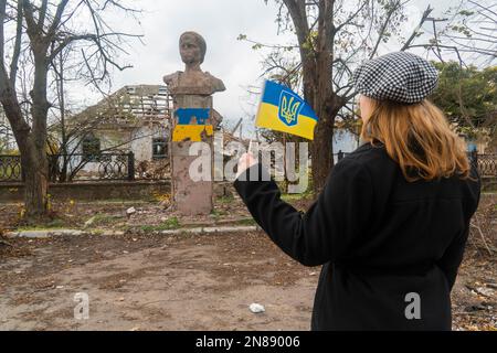 Girl with the flag of Ukraine in her hands looks at the monument damaged by shelling. War in Ukraine. Russian invasion of Ukraine. War crimes Stock Photo