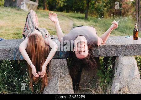 Couple lying in the park, enjoying the time together. Boyfriend smoking, looking upside down Stock Photo