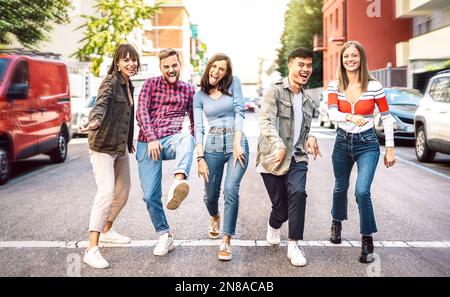 Happy diverse students walking at city center acting funny crazy moves - Trendy guys and girls having fun by urban streets on party mood Stock Photo