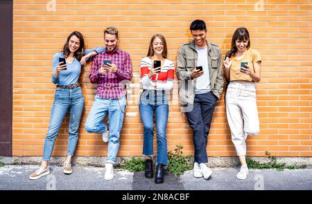 Multicultural tech friends having fun on mobile cell phone devices at urban city place - Young happy men and women sharing time together watching tren Stock Photo