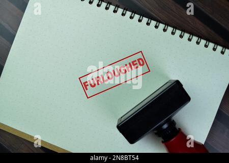 Concept of Red Handle Rubber Stamper and Furloughed text isolated on on Wooden Table. Stock Photo