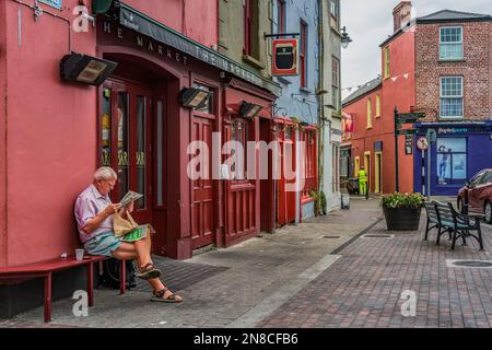 Man reading morning newspaper beside the pub at Market Square in the town centre of Kinsale, co Cork, Ireland. Stock Photo