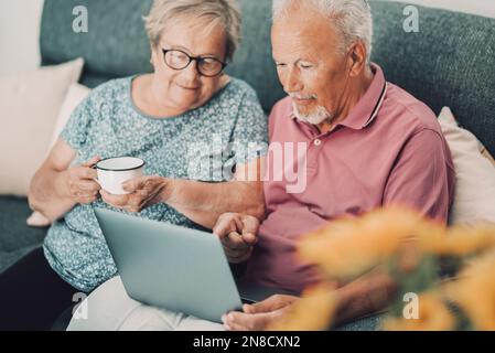 Serene 80s real couple at home using modern laptop technology with internet connection surfing the web and enjoying time and indoo rleisure activity. Stock Photo
