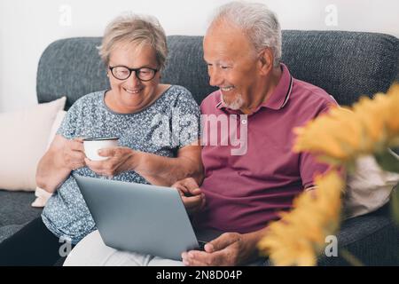 Senior retired happy couple embracing using laptop together, smiling elderly family reading news, shopping online at home, older people and computer o Stock Photo