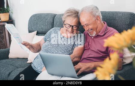 Aged couple at home paying bills on line with laptop and laughing a lot having fun together. Happiness and elderly lifestyle. Man and woman old senior Stock Photo