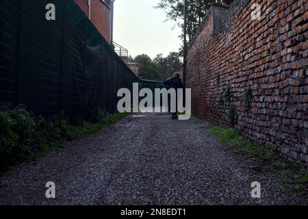 People  walking on a path next to a brick wall at sunset Stock Photo
