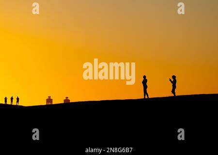 Sunset at Maspalomas Dunes - people shadows at clear sky at sunset. Black suface with yellow orange background. Stock Photo