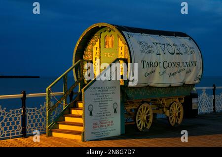 Tarot reader Romany caravan or gypsy wagon lit up by lamp posts at dusk on the boardwalk of Brighton Palace Pier, East Sussex, England, UK Stock Photo