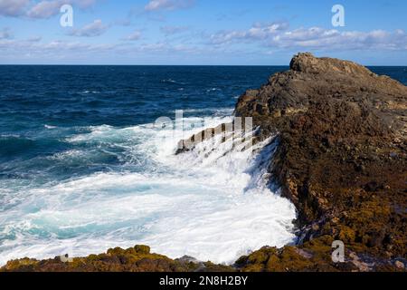 Nature's Fury: The ocean's waves hitting rocks on the shore at daylight with some clouds above. Stock Photo