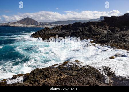 Nature's Fury: The ocean's waves hitting rocks on the shore at daylight with some clouds above. Stock Photo