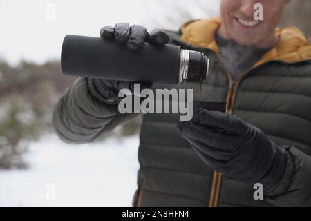 Man pouring hot drink from thermos into cap outdoors on snow day, closeup Stock Photo