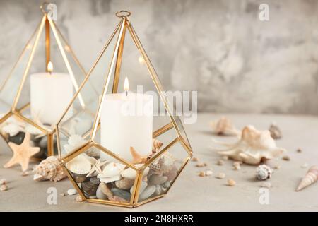 Stylish glass holders with burning candles, seashells and pebbles on light stone table Stock Photo