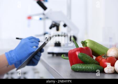 Fresh vegetables on table, scientist proceeding quality control in laboratory Stock Photo