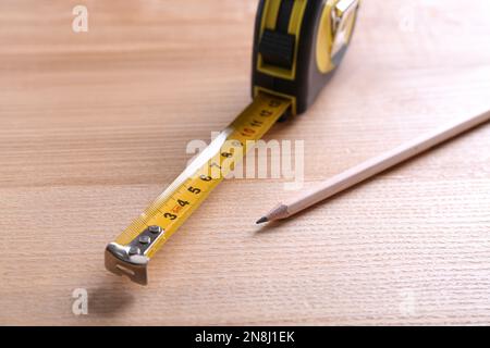 Self retracting metal measuring tape and pencil on wooden table, closeup Stock Photo