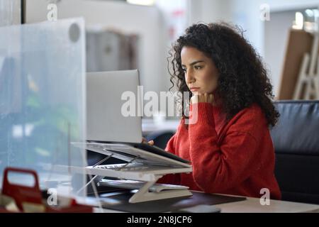 Busy latin female worker working on laptop thinking analyzing online data. Stock Photo