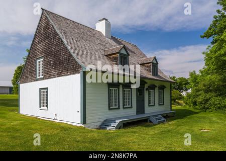 Old 1809 French regime cottage style home facade with white planked wood siding, grey trim white windows and cedar shingles roof in late spring. Stock Photo