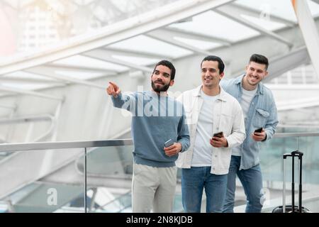 Group Of Guys Using Phones Pointing Finger Aside In Airport Stock Photo