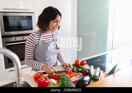 Cheerful hispanic woman enjoying cooking at home, using digital tablet Stock Photo