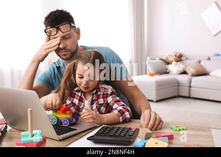 Cute child disturbing stressed man in living room. Working from home during quarantine Stock Photo