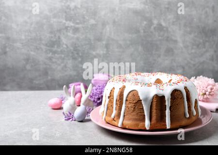 Glazed Easter cake with sprinkles, painted eggs and flowers on grey table, space for text Stock Photo