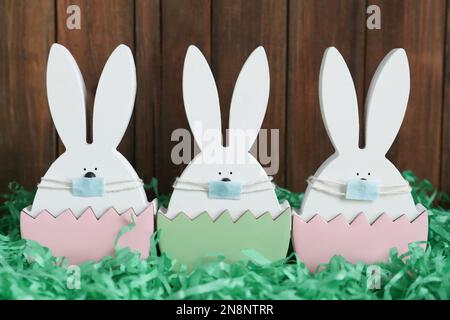 Cute bunny figures in protective masks on wooden background. Easter holiday during COVID-19 quarantine Stock Photo