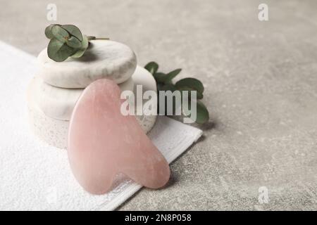 Rose quartz gua sha tool, spa stones and eucalyptus branches on grey table, space for text Stock Photo