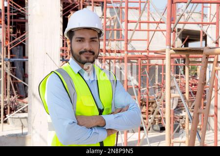 Portrait of young man is engineer wearing helmet smile with satisfied at construction site, architect or contractor standing and arms crossed with con Stock Photo