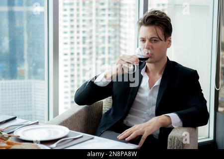 Young caucasian businessman in suit drinking red wine and sitting at the restaurant luxury on skyscraper, handsome business man drinking champagne or Stock Photo