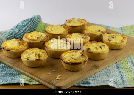 Many mini ham and cheese quiches on wooden kitchen cutting board Stock Photo
