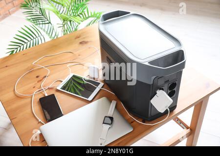 Portable power station charging gadgets on table in room Stock Photo